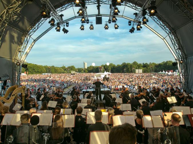Orchester spielt auf Open-Air-Bühne vor großer Menschenmenge