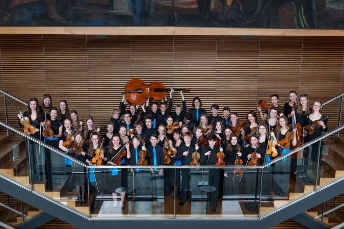 A group of young people with string instruments on a staircase