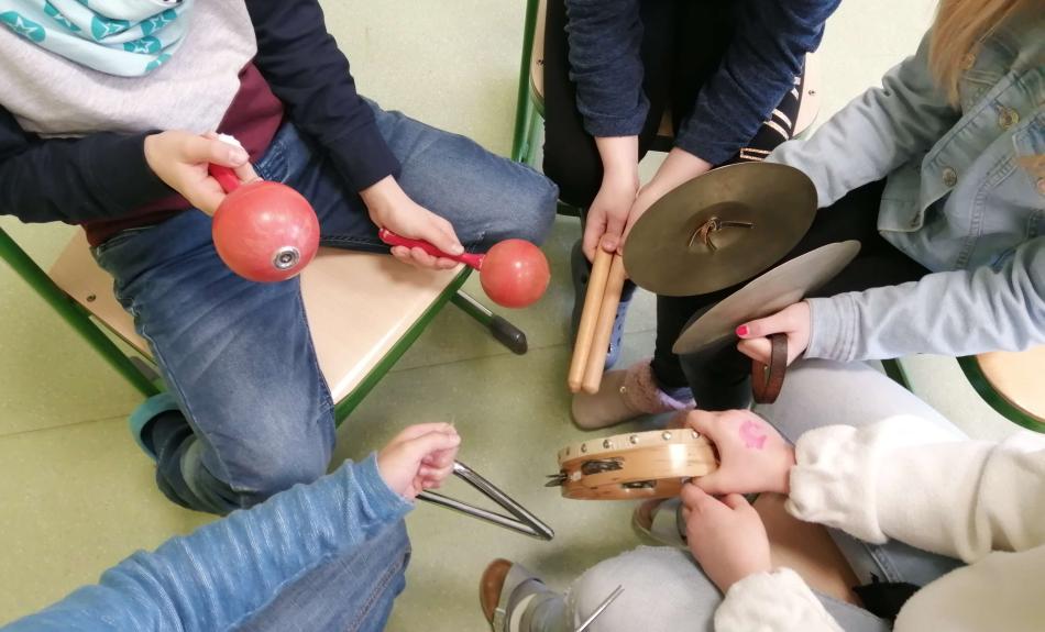 Musikunterricht an der Marienschule in Bad Hönningen. Aus der Vogelsicht kann man in den Stuhlkreis von fünf Kindern schauen, die verschiedene Schlag- und Rhythmusinstrumente in den Händen halten.