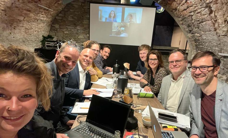 Eine Gruppe Menschen mit Laptops und Notizblöcken sitzen an Tisch in Kellergewölbe