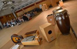 Weiterbildung an der Landesmusikakademie NRW: Im Vordergrund sind mehrere Musikinstrumente zu sehen, eine große Gruppe Teilnehmer*innen im Hindergrund.