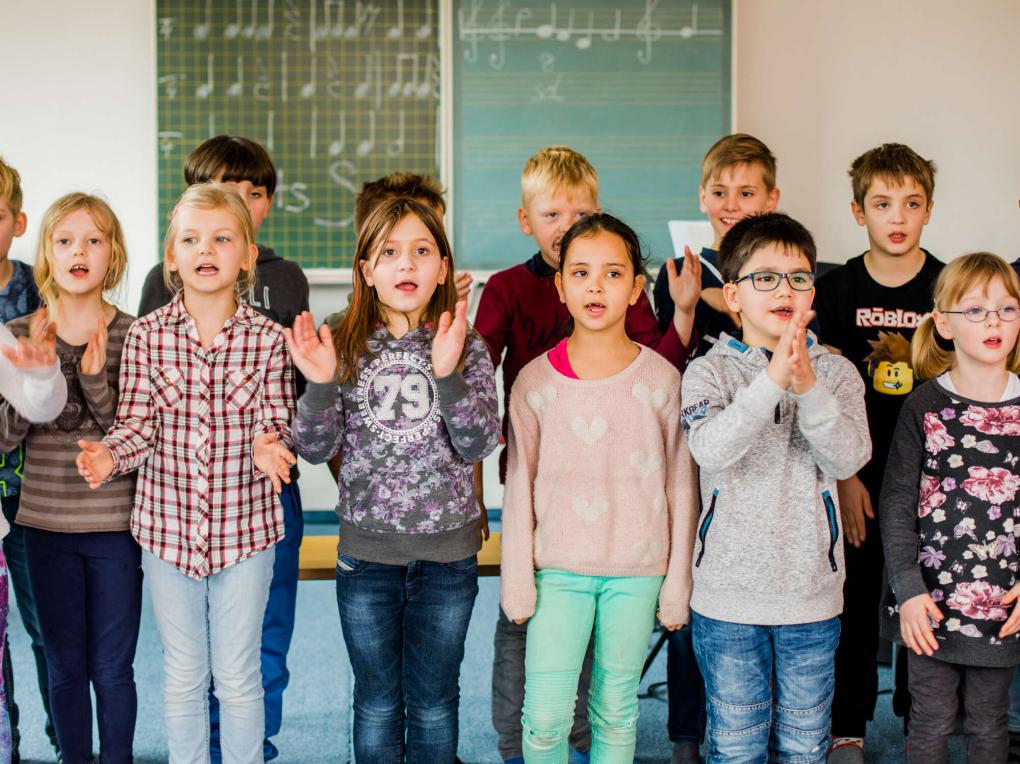 A children's choir is singing in front of a blackboard in the classroom