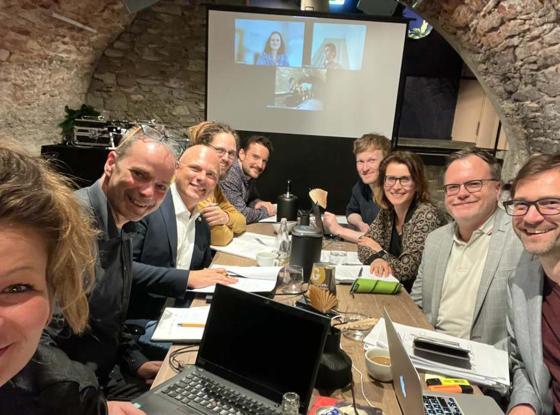 Eine Gruppe Menschen mit Laptops und Notizblöcken sitzen an Tisch in Kellergewölbe